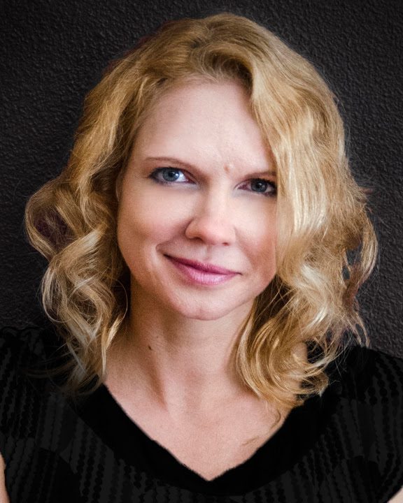 Blonde woman with wavy hair, smiling slightly.